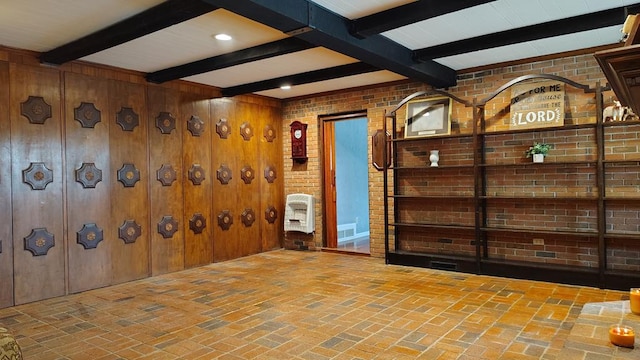 empty room featuring brick floor, beamed ceiling, and brick wall