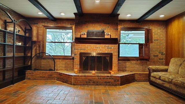 living room featuring beamed ceiling, brick floor, brick wall, and a healthy amount of sunlight