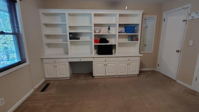 unfurnished office featuring baseboards, built in desk, visible vents, and carpet floors