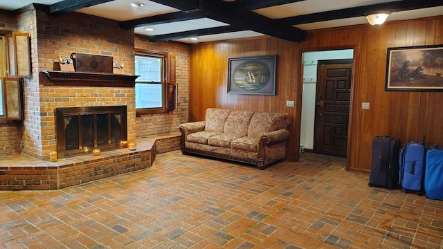 living area featuring beamed ceiling, brick floor, wood walls, and a brick fireplace