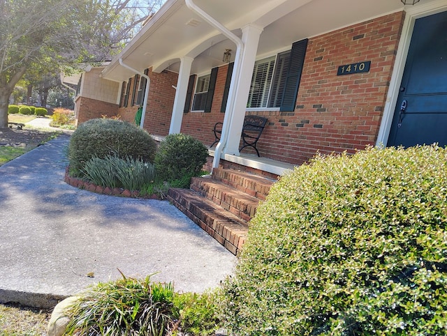 entrance to property featuring covered porch and brick siding