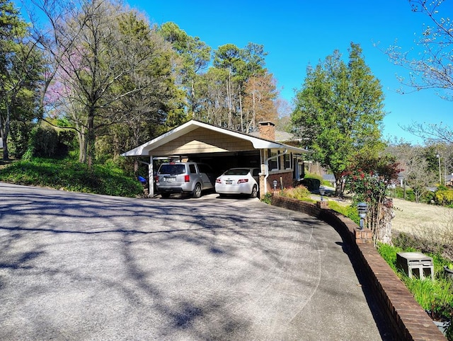 view of property exterior with a chimney, a detached carport, and aphalt driveway