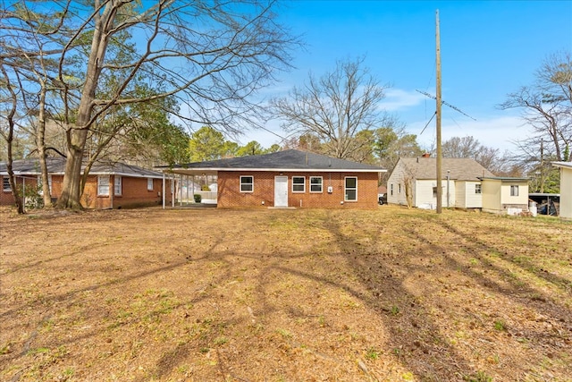 rear view of house featuring a carport, brick siding, and a yard