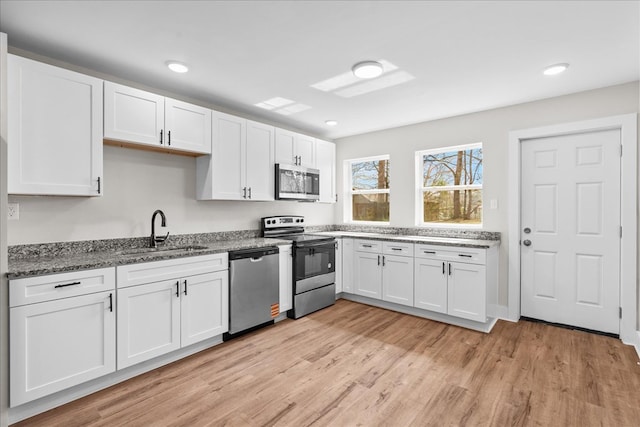 kitchen with appliances with stainless steel finishes, stone countertops, white cabinetry, a sink, and light wood-type flooring