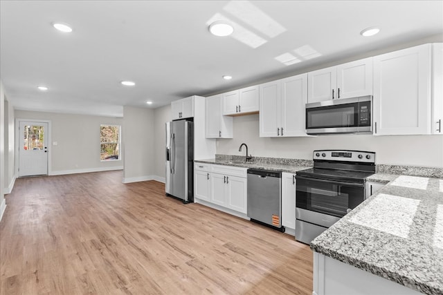 kitchen featuring white cabinets, appliances with stainless steel finishes, light stone countertops, light wood-type flooring, and a sink