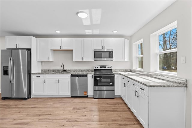 kitchen featuring appliances with stainless steel finishes, white cabinetry, a sink, and light wood finished floors