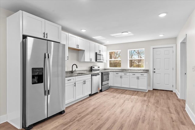 kitchen featuring stainless steel appliances, light wood-type flooring, white cabinets, and a sink