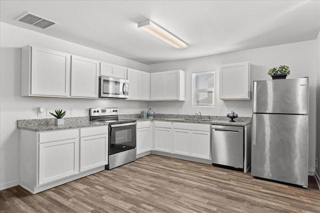 kitchen featuring appliances with stainless steel finishes, white cabinetry, sink, light stone countertops, and light hardwood / wood-style flooring