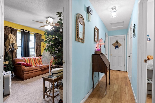 hallway featuring light wood-style floors, a textured ceiling, and baseboards