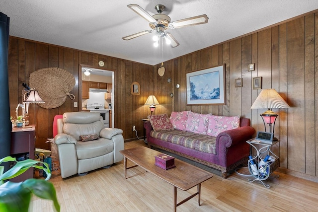 living room featuring wooden walls, a ceiling fan, and light wood-style flooring
