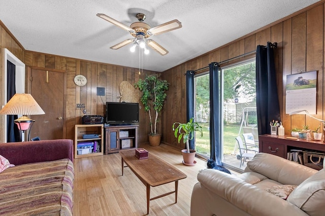 living area featuring a textured ceiling, ceiling fan, wood walls, and light wood finished floors