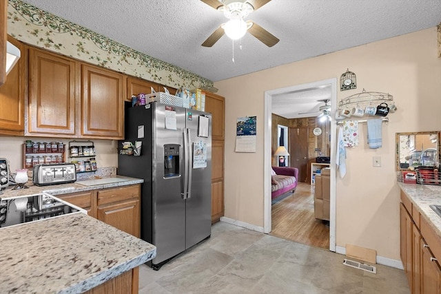 kitchen featuring stainless steel fridge, ceiling fan, brown cabinets, and a textured ceiling