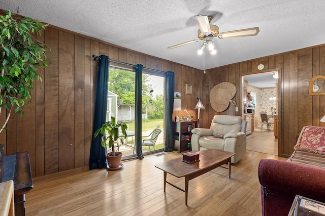 living room with wooden walls, a textured ceiling, ceiling fan, and light wood-type flooring