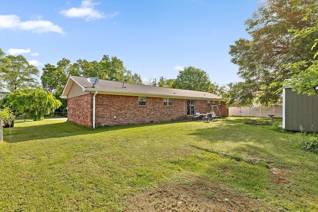 rear view of house with crawl space, brick siding, fence, a storage unit, and a yard
