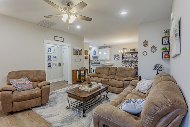 living area featuring ceiling fan with notable chandelier, light wood-type flooring, visible vents, recessed lighting, and baseboards