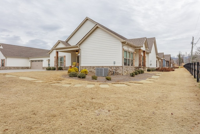 view of property exterior featuring roof with shingles, fence, an attached garage, concrete driveway, and central AC unit