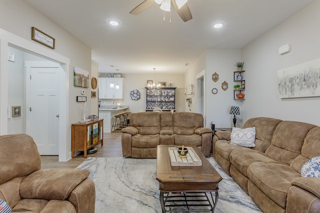 living area with light wood-style flooring, recessed lighting, and ceiling fan with notable chandelier