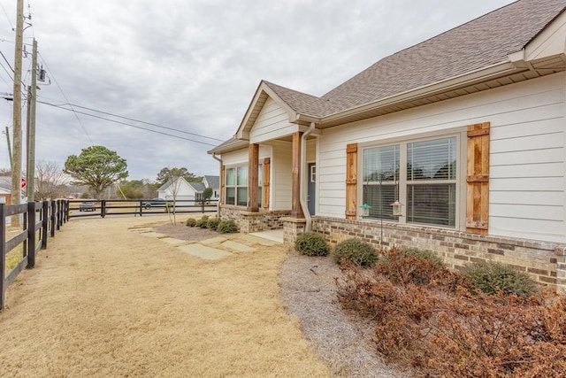view of side of home with brick siding, fence, and a shingled roof