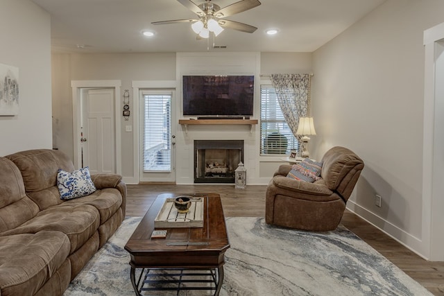 living area featuring wood finished floors, a fireplace, a ceiling fan, and baseboards