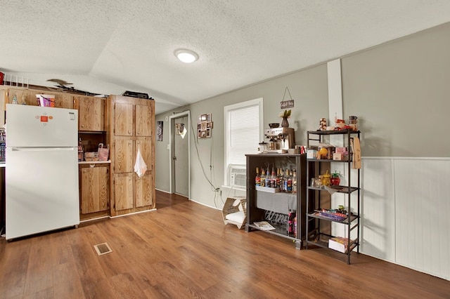 kitchen with wood-type flooring, vaulted ceiling, white fridge, and a textured ceiling