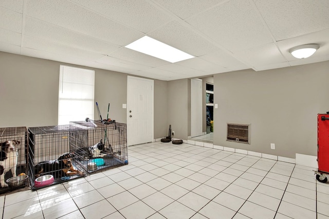 basement featuring heating unit, light tile patterned floors, and a drop ceiling