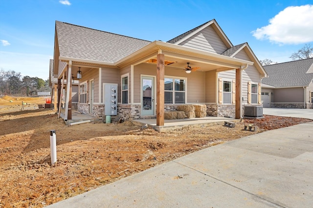 view of front of house featuring driveway, a ceiling fan, roof with shingles, central air condition unit, and brick siding