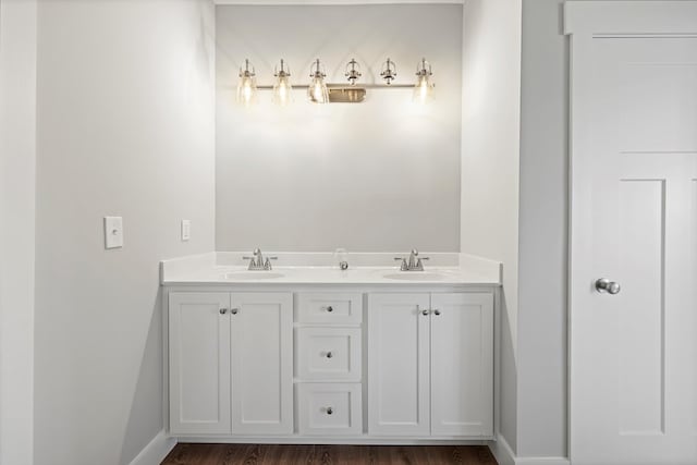 bathroom with wood finished floors, a sink, baseboards, and double vanity