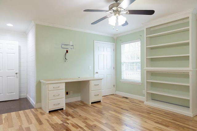 unfurnished office featuring ceiling fan, ornamental molding, built in desk, and light wood-type flooring