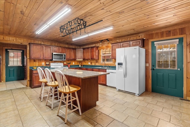 kitchen with sink, wood ceiling, white appliances, a kitchen island, and wood walls