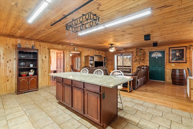 kitchen featuring wooden ceiling, wooden walls, a kitchen breakfast bar, a kitchen island, and ceiling fan