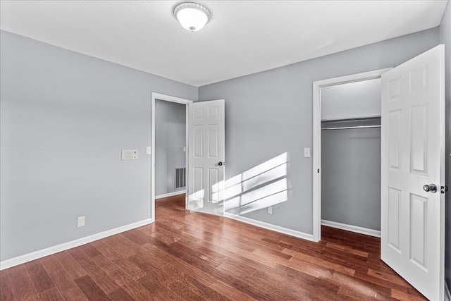 unfurnished bedroom with dark wood-type flooring, a spacious closet, and a closet