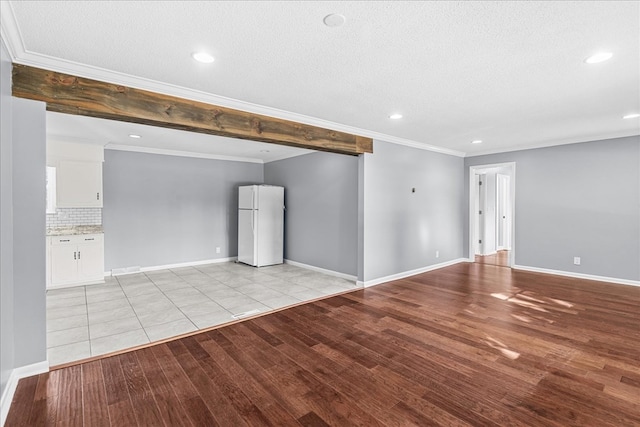 unfurnished room featuring beamed ceiling, crown molding, a textured ceiling, and light hardwood / wood-style flooring