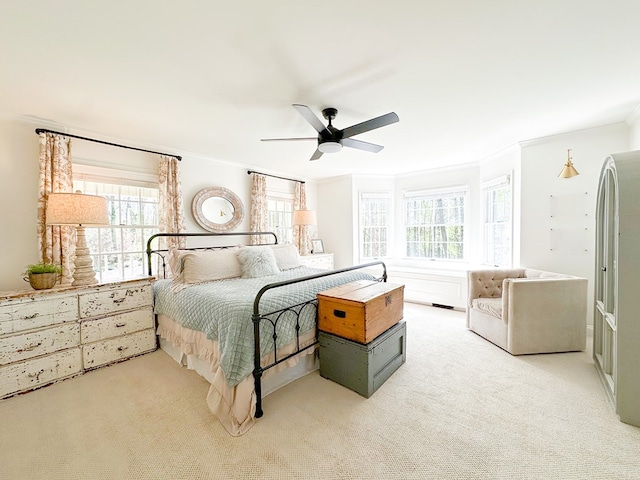 bedroom featuring ornamental molding, multiple windows, light colored carpet, and a ceiling fan