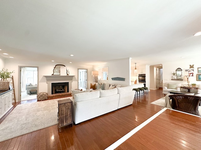 living room with arched walkways, recessed lighting, a fireplace with raised hearth, and wood-type flooring