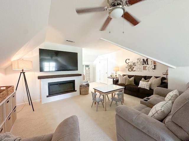 carpeted living room featuring a glass covered fireplace, visible vents, vaulted ceiling, and a ceiling fan
