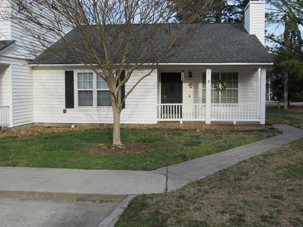 view of front of home featuring a porch, a front yard, roof with shingles, and a chimney