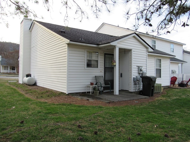 rear view of house featuring a shingled roof, central AC unit, a lawn, a patio, and a chimney