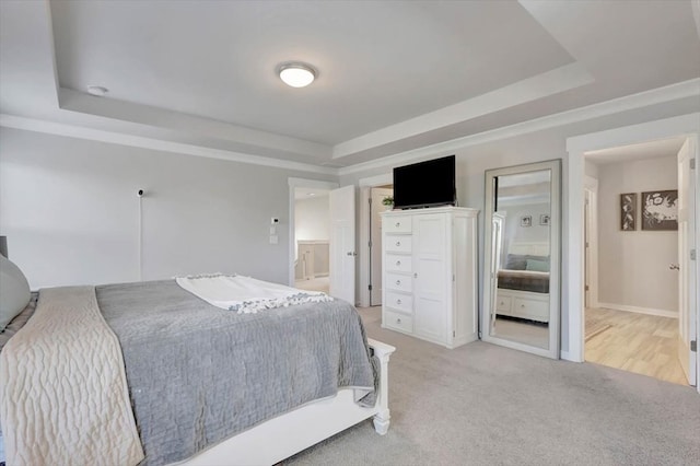 bedroom with a raised ceiling, connected bathroom, and light colored carpet