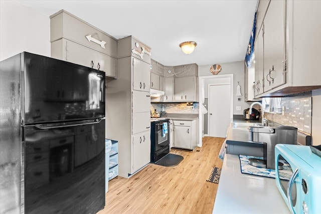 kitchen featuring light wood-type flooring, sink, decorative backsplash, and black appliances