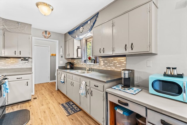 kitchen with range, sink, decorative backsplash, and light wood-type flooring