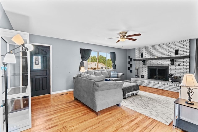 living room with a brick fireplace, ceiling fan, and light wood-type flooring