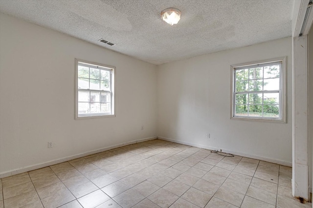 empty room featuring a healthy amount of sunlight, light tile patterned floors, and a textured ceiling