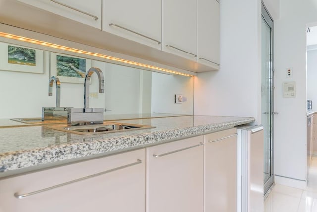 kitchen with light stone counters, white cabinetry, and sink