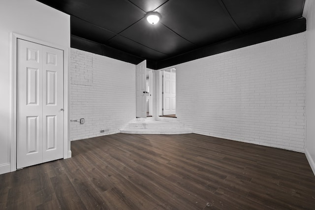 unfurnished room featuring brick wall and wood finished floors