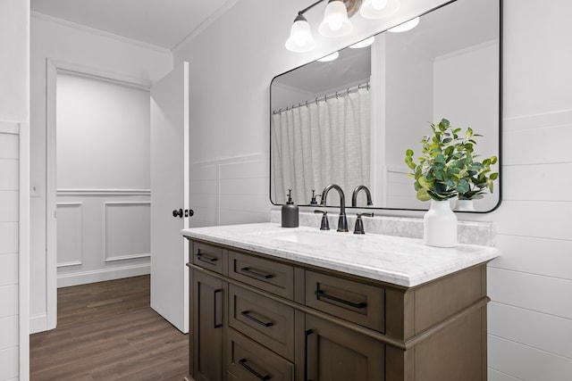 bathroom with wood finished floors, crown molding, vanity, and wainscoting
