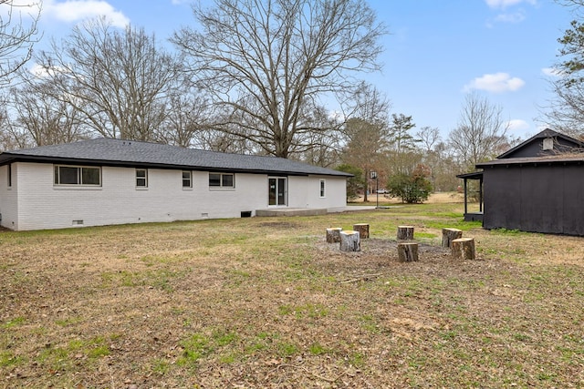 rear view of house with crawl space, brick siding, and a lawn