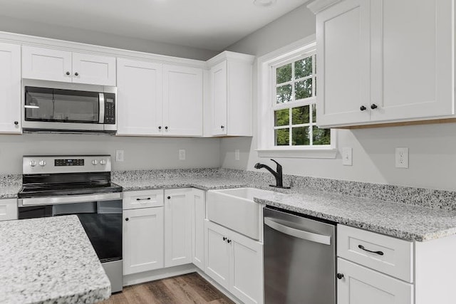 kitchen with sink, appliances with stainless steel finishes, light stone counters, white cabinets, and dark hardwood / wood-style flooring