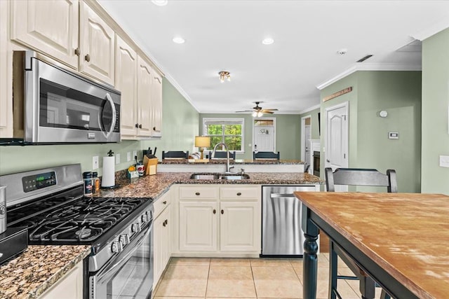 kitchen featuring sink, dark stone counters, kitchen peninsula, stainless steel appliances, and crown molding