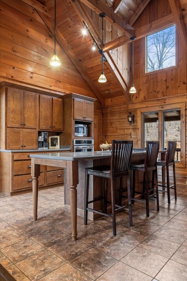 kitchen with appliances with stainless steel finishes, wood walls, beamed ceiling, hanging light fixtures, and wooden ceiling