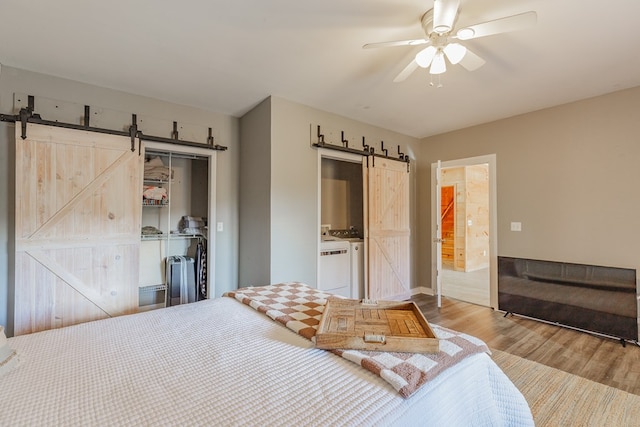 bedroom featuring wood-type flooring, a closet, ceiling fan, a barn door, and washer and clothes dryer